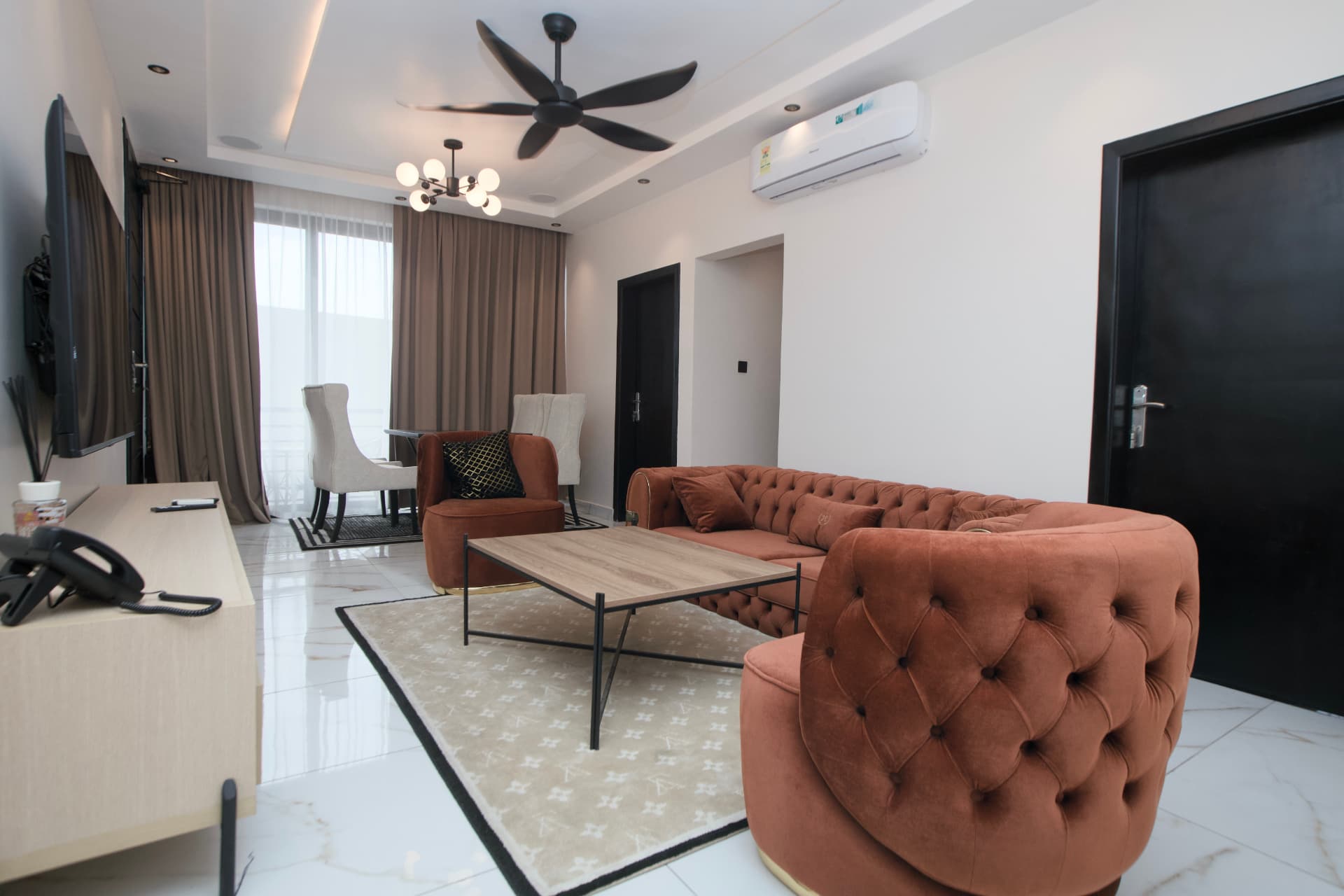 Noir Studio living room with a rust velvet sofa, matching armchairs and a dining nook by the windows